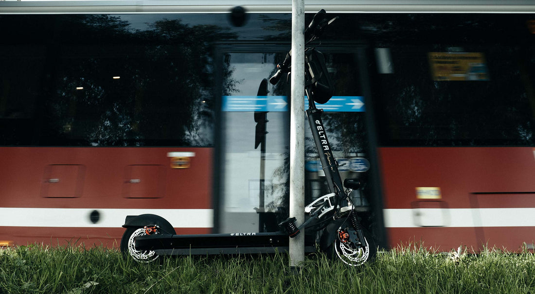 An electric scooter locked to a lamp-post while a red buss drives by behind it