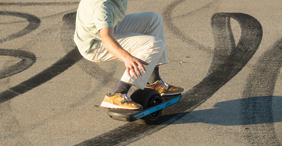 Man in bright clothes rides a onewheel and there are  brake tracks on the ground