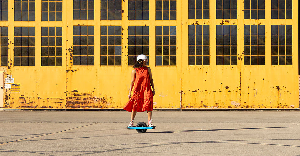 onewheel pint x blue railguards riding by a yellow wall
