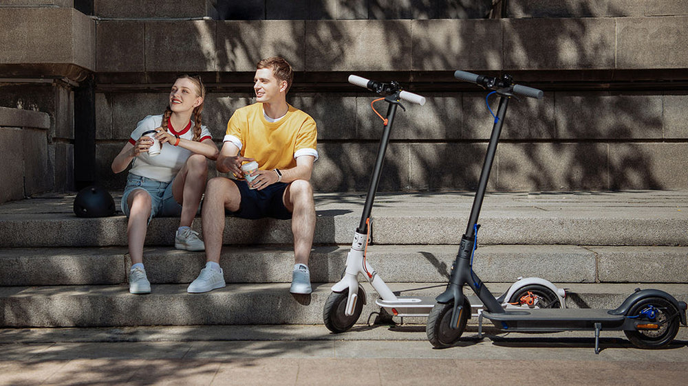 a boy and a girl sitting on the stair outside and next to two electric scooters