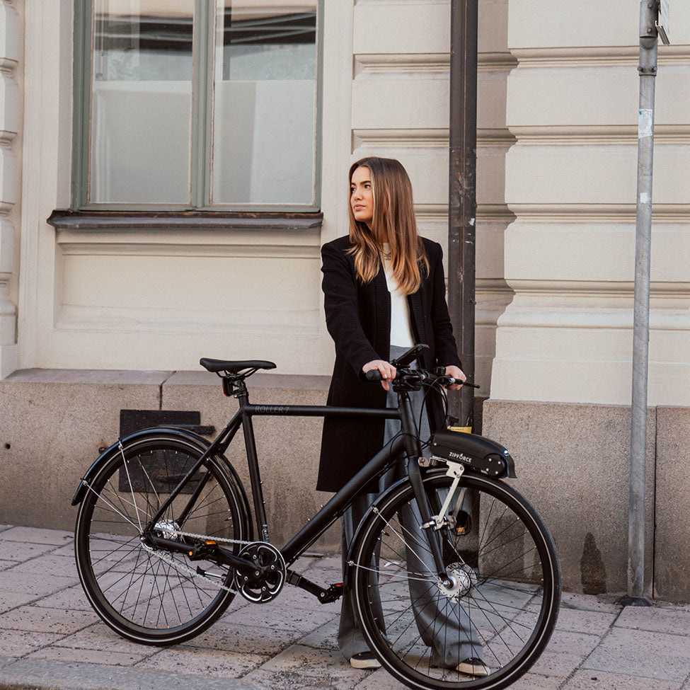 a woman standing in front of a building with a black bicycle and a ziforce mounted on the front wheel