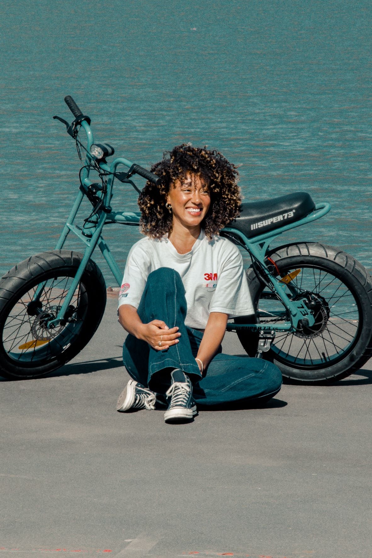 girl sitting on the ground in front of ac super73 bike smiling